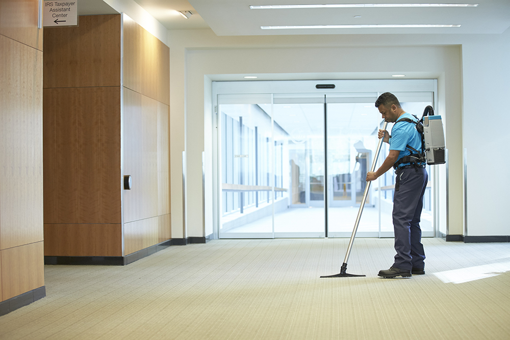 Female cleaning staff vacuuming hallway with backpack